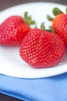 red juicy strawberry in a plate on a wooden surface