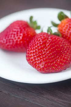 red juicy strawberry in a plate on a wooden surface