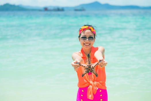 Young woman shows starfish during holiday at tropical island