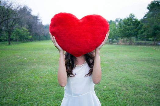 Women holding big love heart shape pillow in the park