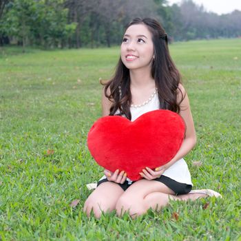 Women holding big love heart shape pillow in the park