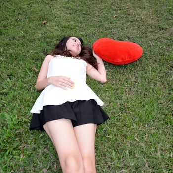 Women holding big love heart shape pillow on green grass