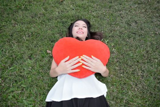 Women holding big love heart shape pillow on green grass