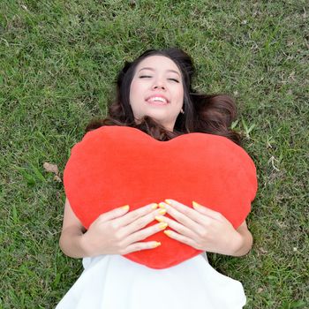 Women holding big love heart shape pillow on green grass