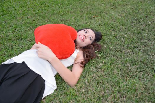 Women holding big love heart shape pillow on green grass