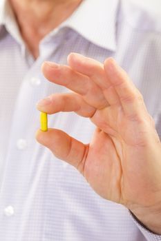 Senior adult man holds medicine capsule in his hand