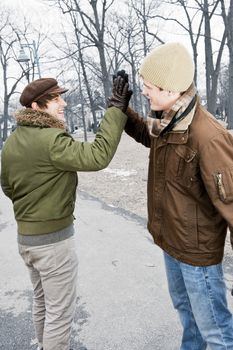 Two young men meeting in winter park giving high five