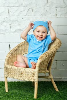 Little boy sitting in a wicker chair on the lawn barefoot