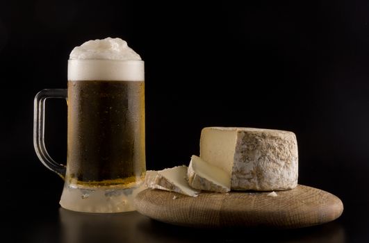 Foaming beer with artisanal goat cheese on wooden board