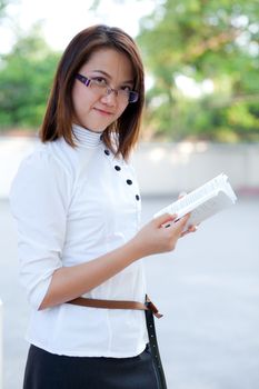 Woman looking you and carry book in hand.
