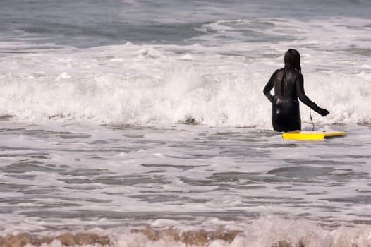 Sports loving person heads out into the surf to ride her board