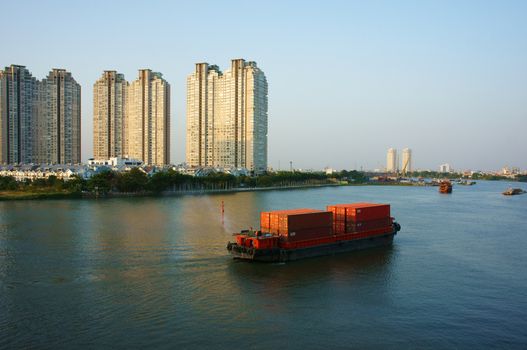 HO CHI MINH CITY, VIET NAM- MARCH 12: Maritime transport on river, vessel loading container on water, residential and apartment at riverside, scene of industrial city, Vietnam, March 12, 2014