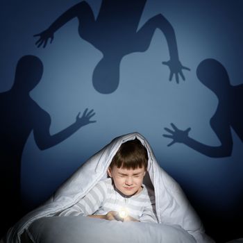 image of a boy under the covers with a flashlight the night afraid of ghosts