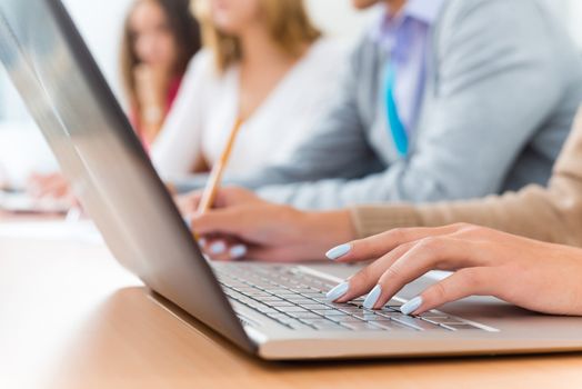 close-up of female hands on the laptop keyboard, students listen to the teacher at the University of