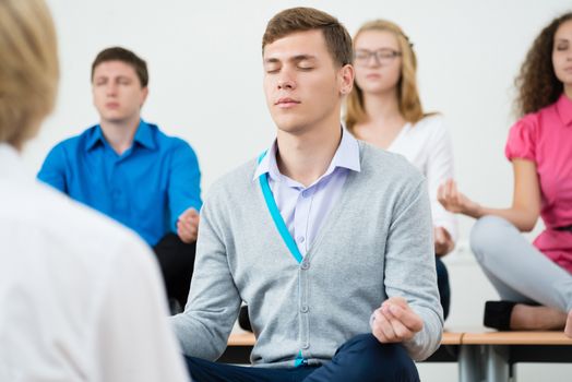 group of young people meditating in office at desk, group meditation