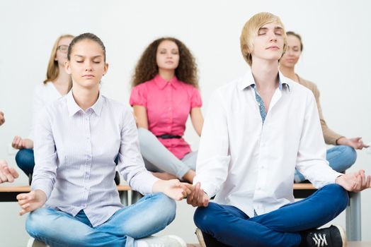 group of young people meditating in office at desk, group meditation