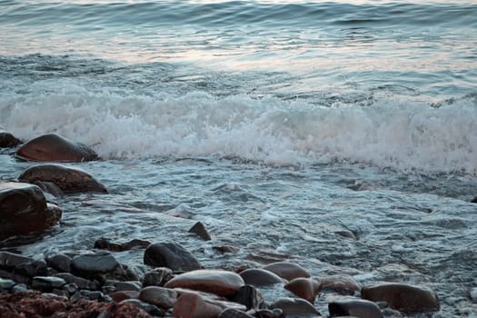 Foamy wave on the stone seashore at sunset