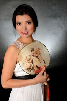 Asian female model wearing white dress. Young Chinese girl holding fan in hand, smiling gently.