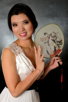 Asian female model wearing white dress. Young Chinese girl holding fan in hand, smiling gently.