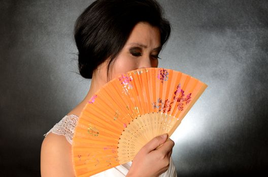 Asian female model wearing white dress. Young Chinese girl holding fan in hand, smiling gently.