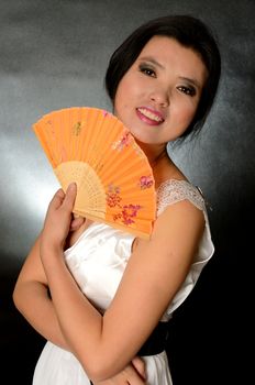 Asian female model wearing white dress. Young Chinese girl holding fan in hand, smiling gently.