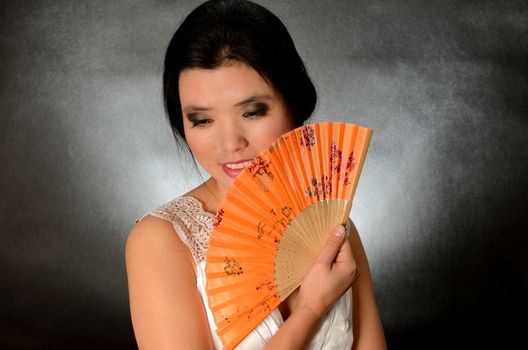 Asian female model wearing white dress. Young Chinese girl holding fan in hand, smiling gently.