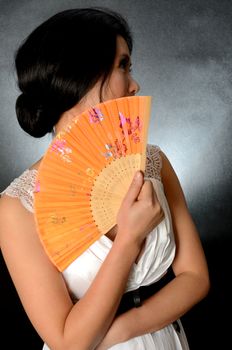 Asian female model wearing white dress. Young Chinese girl holding fan in hand, smiling gently.