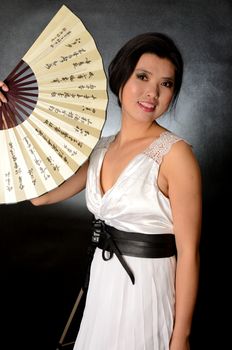 Asian female model wearing white dress. Young Chinese girl holding fan in hand, smiling gently.