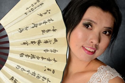 Asian female model wearing white dress. Young Chinese girl holding fan in hand, smiling gently.