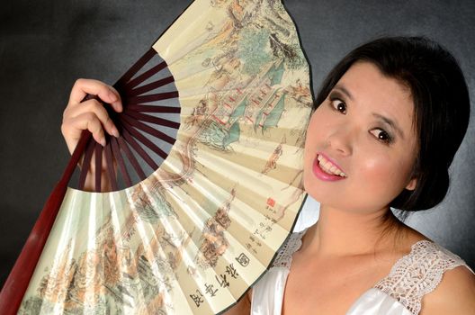 Asian female model wearing white dress. Young Chinese girl holding fan in hand, smiling gently.