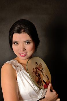 Asian female model wearing white dress. Young Chinese girl holding fan in hand, smiling gently.