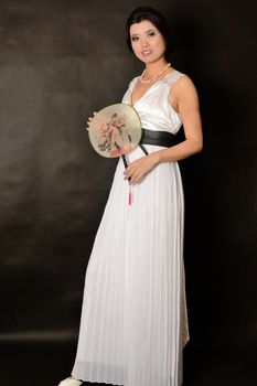 Chinese female wearing long white dress. Asian girl holding fan in her hand, girl with gentle smile.