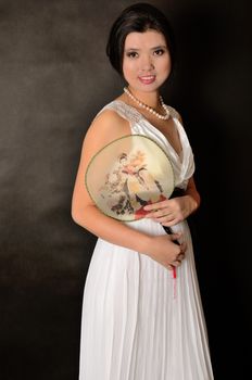 Chinese female wearing long white dress. Asian girl holding fan in her hand, girl with gentle smile.
