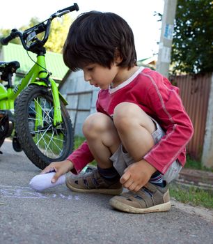 little boy with a bicycle drawing with chalk on asphalt