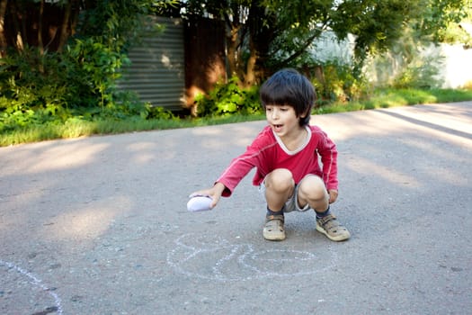 little boy drawing on gray asphalt