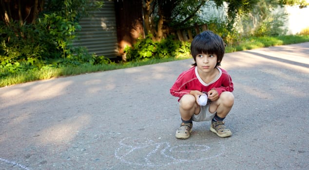 little boy drawing on gray asphalt