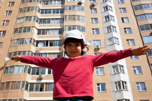 smiling boy threw his arms against the high-rise building