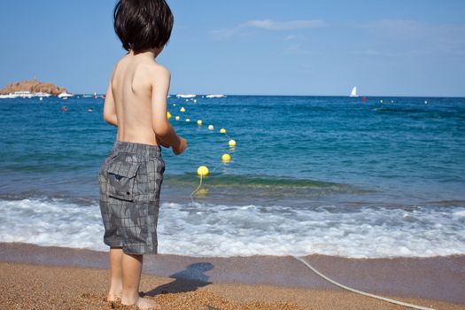 boy standing on the shore looking at the blue sea