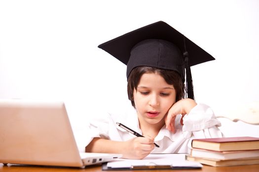 little boy in hat with computer and textbooks on white background writing on paper