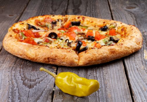 Hot Vegetarian Pizza with Tomatoes, Black Olives and Jalapeno Pepper closeup on Rustic Wooden background