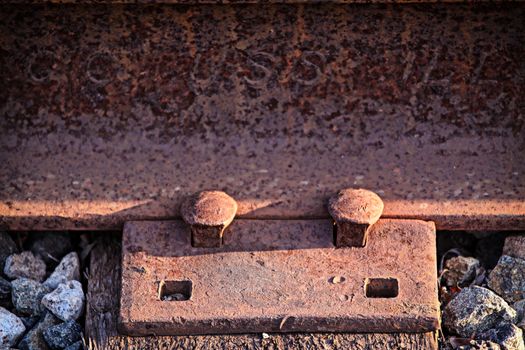 Two rusty old nails fastening a train track.