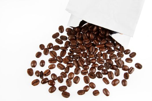 Closeup of coffee beans spilling from packet on plain background