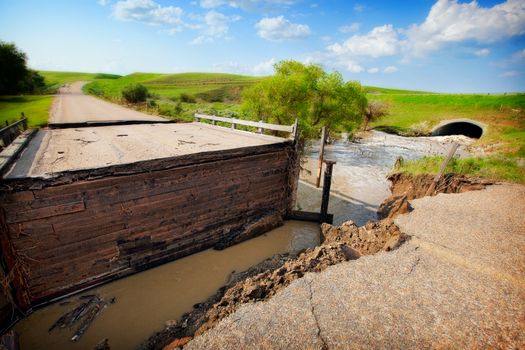 A road and bridge damaged by muddy, flood waters.