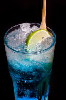 glass of blue cocktail with lime on black background