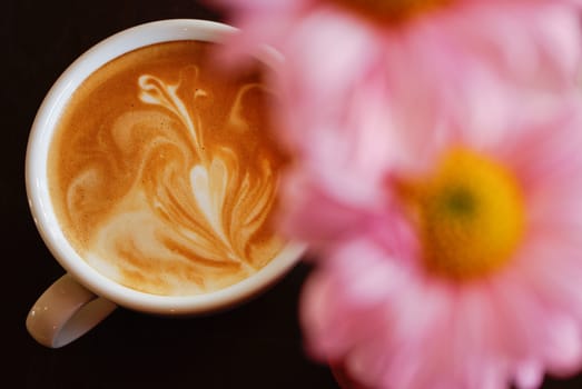 White cup of coffee with pink flower on black