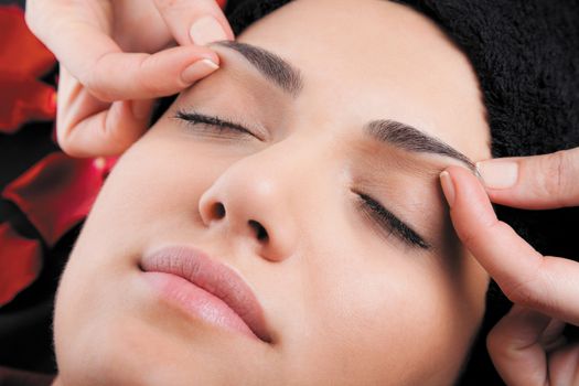 Beautiful woman receiving a facial massage lying on bed with rose petals.