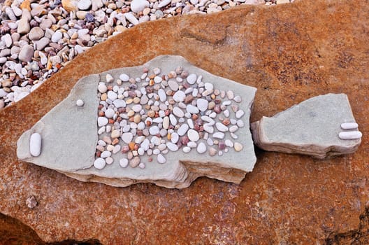 Stone fish symbol of pebbles on the sea boulder