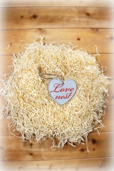 single wooden love heart in a love nest made of straw on floor boards