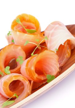 Snack of Swirled Slices of Delicious Smoked Sturgeon with Greens on Wooden Plate closeup on white background