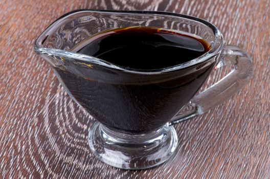 Soy Sauce in in Glass Gravy Boat isolated on Wooden background